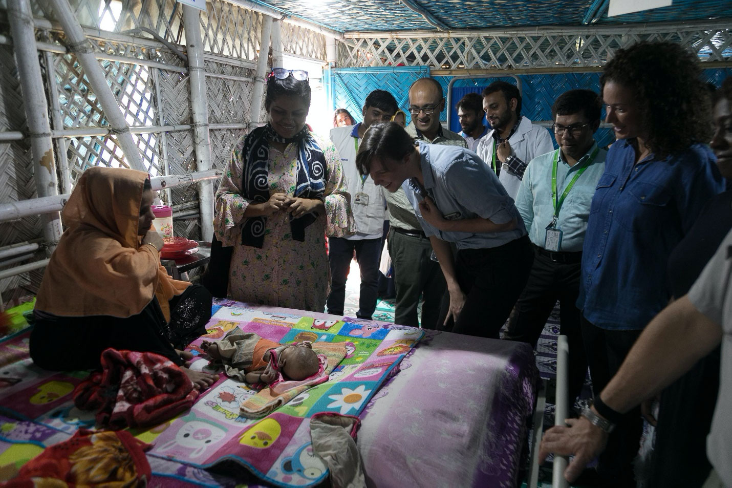 People standing around a mother and her infant on a bed.